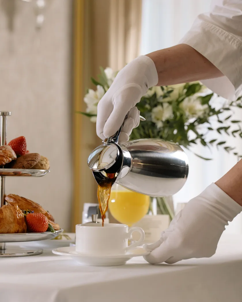 A server in white gloves pouring coffee at a laid table